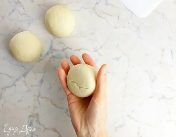 Переворачиваем швом вниз и катаем колобок из теста круговыми движениями по столу. Шов внизу шарика должен исчезнуть. Кладем готовые шарики теста на смазанный маслом противень на расстоянии друг от друга и накрываем пленкой. Даем тесту подняться в два раза (50–80 минут).