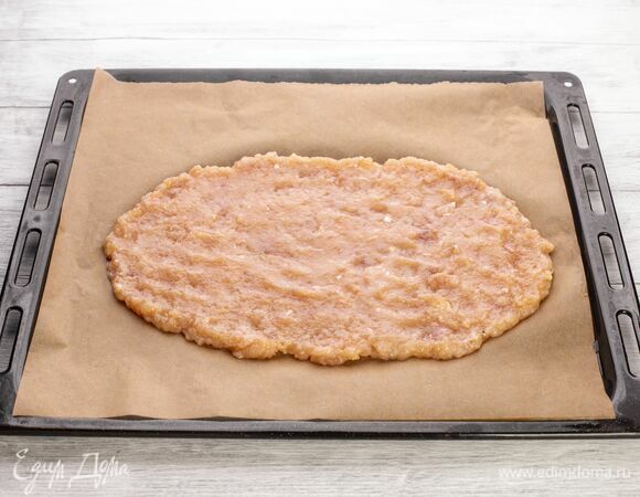 Распределите куриную массу по противню, застеленному пекарской бумагой, в виде тонкой лепешки.