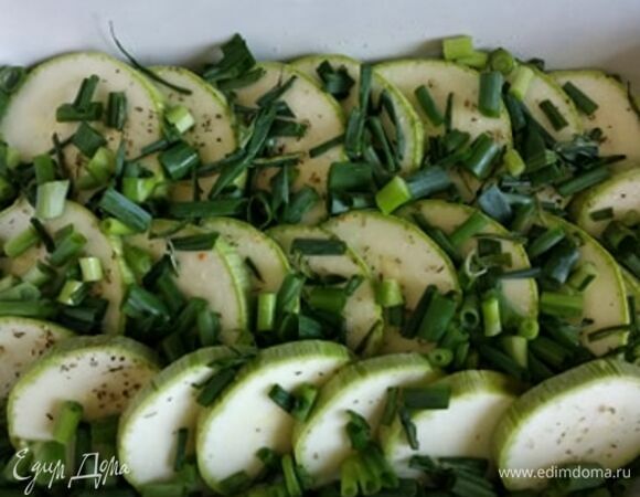 Нарезать зеленый лук. В форму для запекания, смазанную оливковым маслом, выложить кружки кабачка внахлест. Чуть-чуть посолить и поперчить. Посыпать зеленым луком.