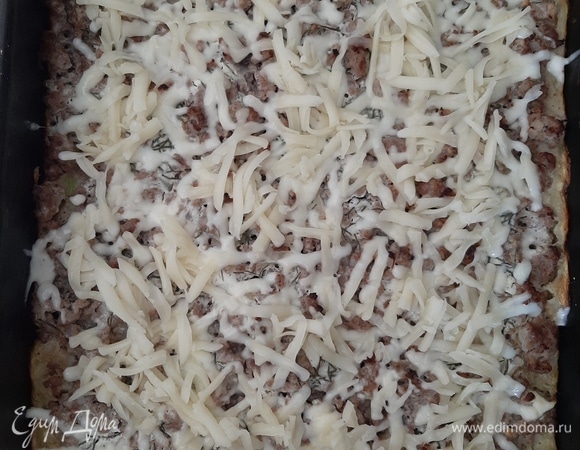 Через 20 минут достаем пиццу из духовки, посыпаем тертым сыром и ставим обратно в духовку на 10 минут.