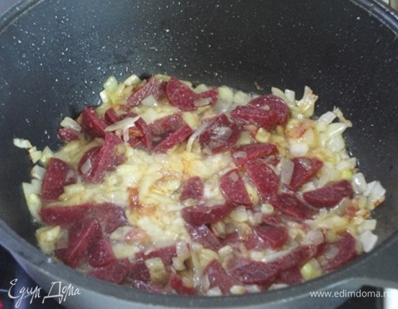 Курицу переложить в тарелку, а в кастрюлю выложить нарезанный кубиками лук. Тушить, помешивая, до мягкости лука. Чоризо нарезать полукружочками и тушить вместе с луком минуты 3.