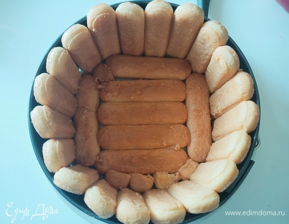 На круглое блюдо ставим кольцо от разъемной формы (22–24см). Вокруг бортов выставляем печенье савоярди так, чтобы сторона с сахаром была снаружи, предварительно окунув его в персиковый сок. Таким же способом укладываем печенье на дно формы.