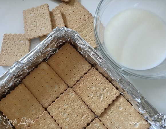 Форму застелить пищевой пленкой или фольгой. Выложить слой печенья, предварительно окунув его в молоко.