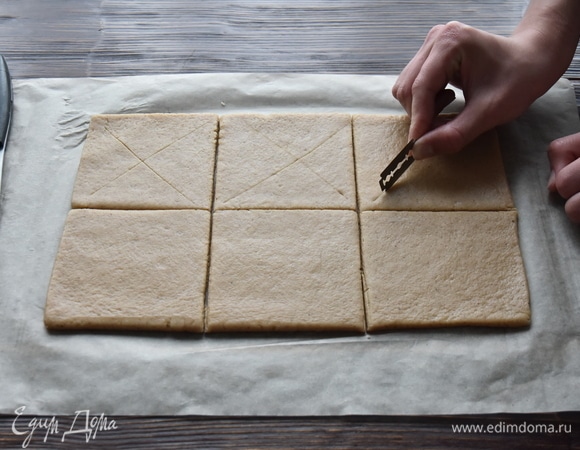 В середине каждого квадрата сделать надрезы крест-накрест, не прорезая тесто до конца.