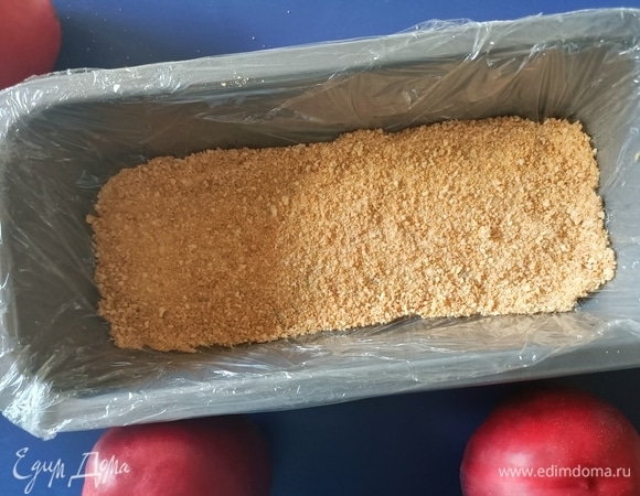 Форму застелить пищевой пленкой. Измельчить печенье, выложить немного на дно формы.