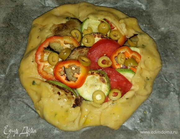 Выложить на тесто подготовленные овощи и оливки, нарезанные колечками. Свернуть края галеты, смазать взбитым яйцом и убрать в разогретую духовку на 30–35 минут при 180°C.