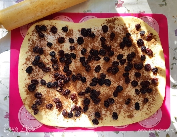 Тесто должно увеличиться в объеме в два раза. Раскатать тесто в форме прямоугольника толщиной 0,5 см. Смазать сливочным маслом, посыпать корицей и изюмом.