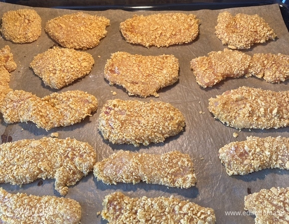 Противень застелить пергаментом. Каждый кусочек обмакнуть в муке, яйце и следом — в кукурузной крошке. Разложить на противне.