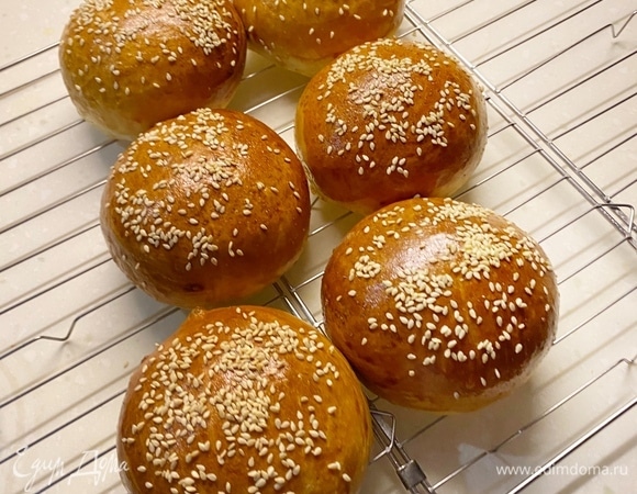 Поделить тесто на шесть равных частей (лучше на весах) и сформировать булочки. Выложить на противень, накрыть пленкой и расстаивать в духовке при 35–40°C примерно 25–35 минут. Они должны увеличиться в два раза. Затем смазать яйцом, посыпать кунжутом и выпекать около 20 минут при 180–190°C, до румяности.