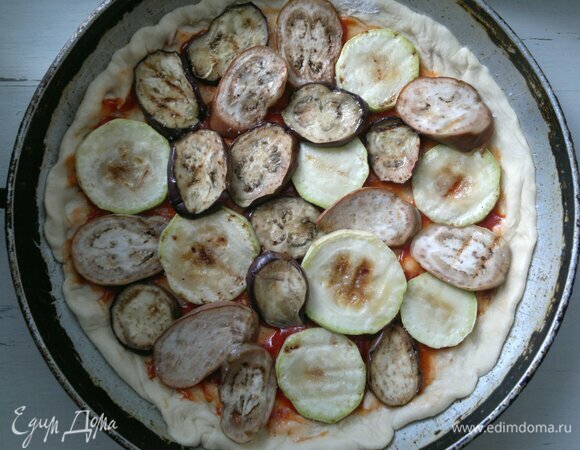 Круг теста смазать томатным соусом, отступая от края 1,5–2 см. Затем выложить обжаренные кружки овощей. Немного посолить и поперчить.