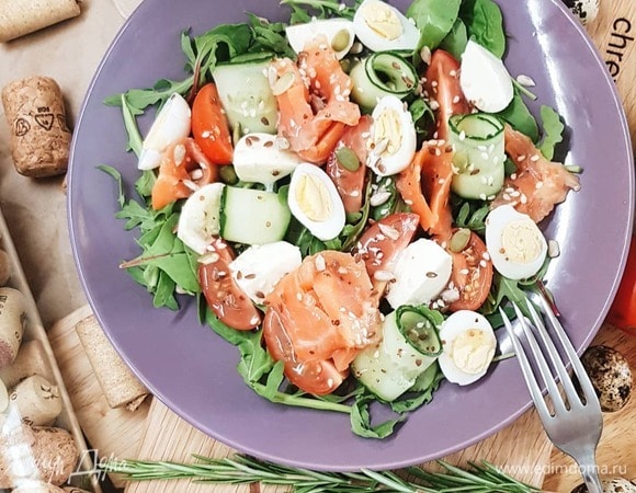 Выложите на блюдо микс салатов. Вымойте овощи. Черри нарежьте пополам, огурц — слайсами. Немного сбрызните салатную зелень соусом. Скрутите слайсы рыбы и огурцов в розочки, выложите на блюдо. Разрежьте пополам яйца, моцареллу. Добавьте вместе с черри в блюдо к огурцам и рыбе. Сбрызните остатками соуса. Приправьте щепоткой семян по желанию.
