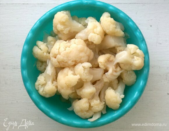 Пока тесто подходит, приготовить начинку. Цветную капусту разделить на соцветия. Отварить до готовности в слегка подсоленной воде. Откинуть на дуршлаг. Затем нарезать на небольшие кусочки.