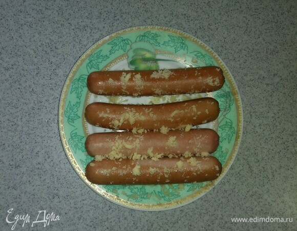 1/3 сыра нужно натереть на самой мелкой терке. Затем слегка остывшие сосиски обвалять в натертом сыре.