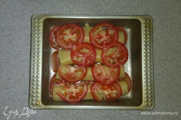 Нарезать кружками еще один помидор. Положить его на сосиски и после этого посыпать помидорные кружки измельченным чесноком.