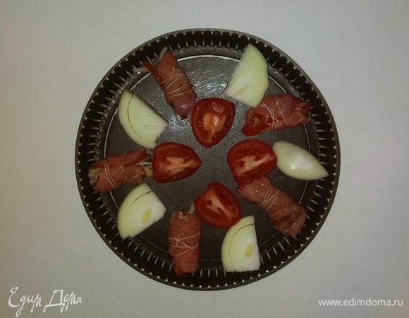 Еще один помидор и вторую половину репчатого лука режем крупными кусочками. Смазываем противень маслом и выкладываем на него мясные рулетики, нарезанный помидор и репчатый лук. Разогреваем духовку до 180°C и ставим в нее противень с мясом и овощами на 30 минут (время приготовления зависит от вашей духовки). При подаче можно украсить листьями петрушки. Приятного аппетита!