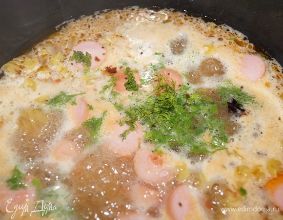 Добавьте в чашу с сосисками макароны, налейте воду (1:2 — часть макарон и две части воды). Жидкость должна прикрывать макароны, тогда будет немного вкусного соуса. Вместо воды можно использовать мясной бульон. Посолите, положите специи и нарезанную зелень, перемешайте все.