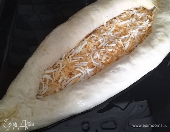 Тем временем натираем на терке сулугуни, российский сыр (можно взять любой другой любимый вами сыр) и смешиваем их. Через час подошедшее тесто делим на 2 части, это будут 2 хачапури. Одну часть раскатываем в блин толщиной 0,5 см и по всей поверхности посыпаем половиной смеси сыров, после чего начинаем скручивать края с двух сторон в рулет, пока не образуется лодочка. Так делать не принято, зато получается очень вкусная хрустящая сырная корочка. Готовую лодочку смазываем взбитым подсоленным яйцом, оставшееся яйцо выливаем в лодочку. Оставляем для расстойки на 30 минут, затем выпекаем в течение 30 минут при 180°C. Приятного аппетита 😊