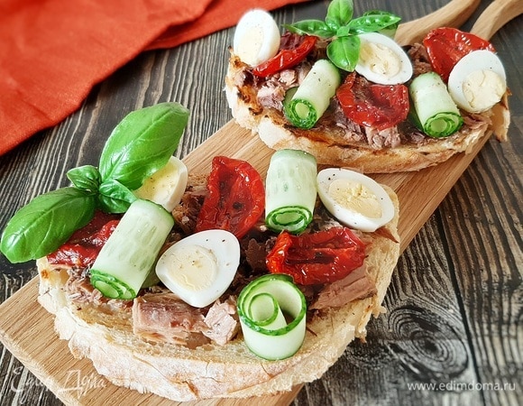 Выкладываем на тост мясо тунца, вяленые томаты, яйцо и рулетики из огурца. Посыпаем свежемолотым черным перцем. Приятного аппетита!