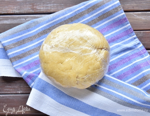 Из получившейся крошки собрать тесто в единый комок. Тесто получается неоднородным и слоистым. Долго месить его не следует, иначе от тепла рук масло начнет таять. Обернуть тесто пленкой и положить в холодильник.
