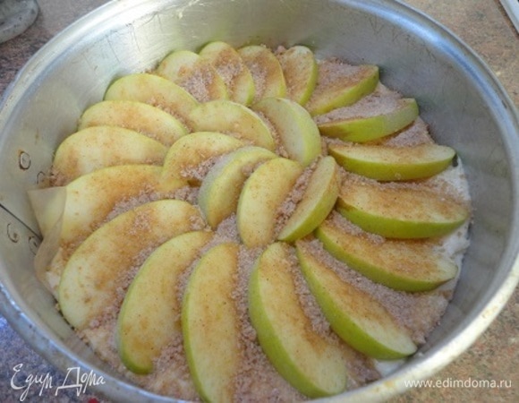 Перелейте тесто в подготовленную форму. Сверху выложите дольки яблок по спирали. Посыпьте смесью коричневого сахара и корицы.