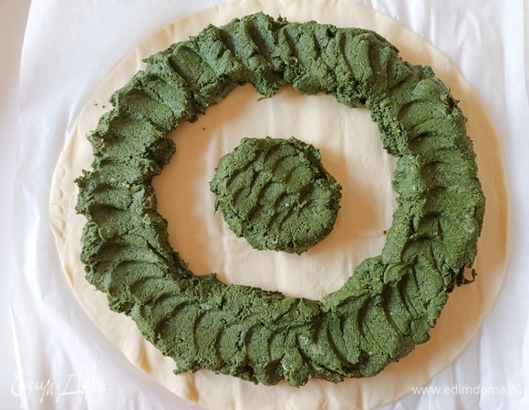 Противень застелить пергаментной бумагой. Раскатываем первый пласт слоеного теста. Выкладываем начинку — немного в центр, остальную по кругу, не доходя до края 1 см.