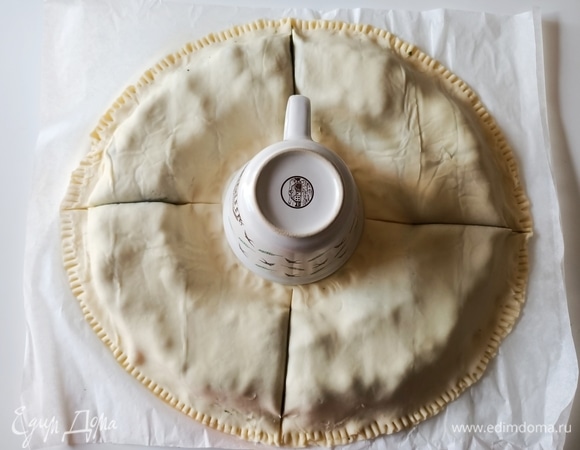 Тесто без начинки смазываем водой и накрываем вторым пластом слоеного теста, защипываем концы. В центр ставим чашку и разрезаем тесто на четыре части.