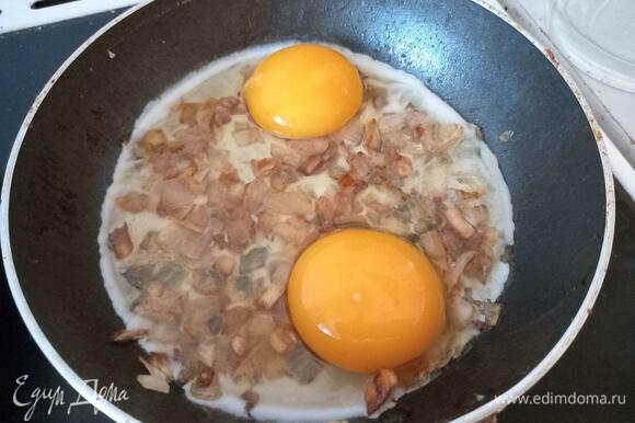 Аккуратно поместить два разбитых яйца на сковороду поверх зажарки из лука и чеснока, не повредив желток.