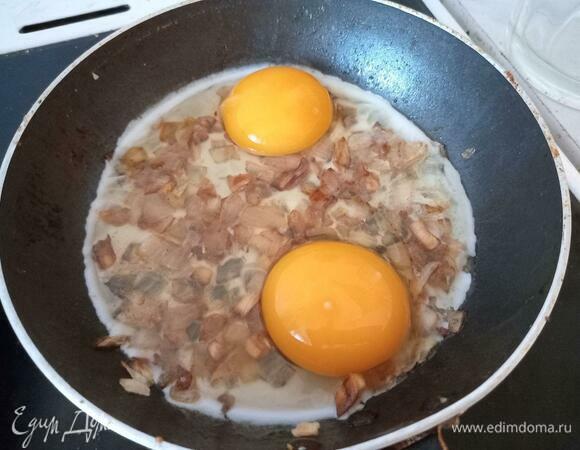 Аккуратно поместить два разбитых яйца на сковороду поверх зажарки из лука и чеснока, не повредив желток.