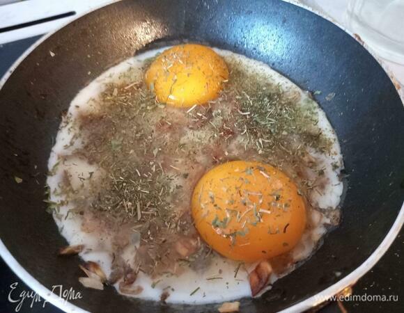Тут же всыпать сушеные травы, стараясь сильно не засыпать желток. Если травы не нравятся, просто пропустите этот шаг. Закрыть крышкой на две минуты, готовить на среднем огне, чтобы схватился белок и сушеные травы немного смягчились.