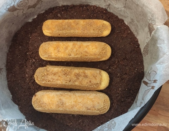 Достаньте форму с основой из духовки. Убавьте температуру в духовке до 170°C. Заварите крепкий кофе, остудите. Ненадолго окуните савоярди в кофе (печенье не должно пропитаться жидкостью полностью). Вплотную уложите печенье на основу торта.