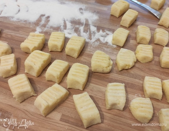 Из остывшего картофеля и мучной смеси замесить тесто, разделить на четыре части, скатать в колбаски, разрезать на кусочки длиной 3 см, слегка придавить вилкой, чтобы придать характерный для ньокков рисунок.