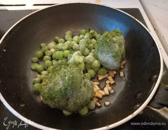 Добавить к чесноку замороженные горошек и шпинат. Закрыть крышкой, оставить на 5 минут. Шпинатные шарики должны расползтись, а горошек стать мягким.