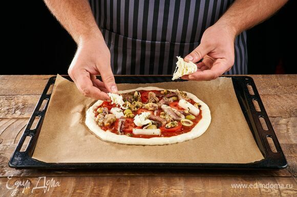 Порвите сыр и выложите на пиццу. Выпекайте в разогретой до 200°C духовке около 12 минут.