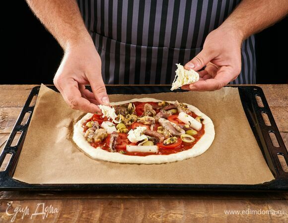 Порвите сыр и выложите на пиццу. Выпекайте в разогретой до 200°C духовке около 12 минут.