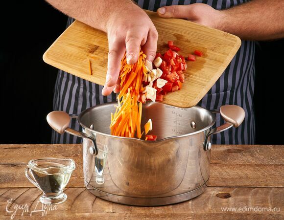 В кастрюлю налейте растительное масло, выложите морковь, чеснок, помидор. Жарьте на небольшом огне, пока морковь не станет мягкой. 