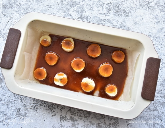 Дно формы выстелить пергаментом, разложить кружочки банана и залить карамелью.