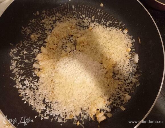 К луку и чесноку высыпаем сырой рис, убавляем огонь до среднего.