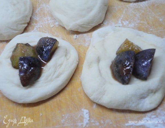 Каждый кусочек теста расплющить руками и выложить по 3 кусочка сливы. Осторожно залепить края и выложить на противень, застеленный пергаментом, швом вниз. Оставить булочки в теплом месте для подъема.