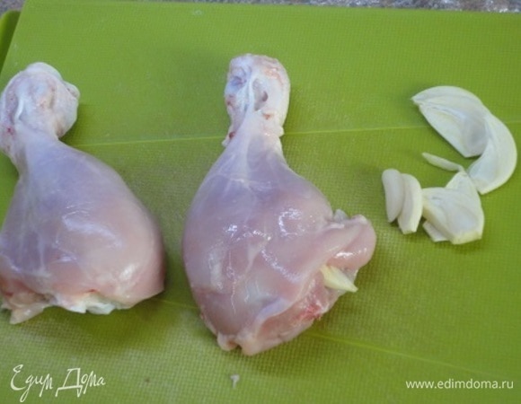 Куриные голени вымыть и просушить бумажными полотенцами. Чеснок нарезать пластинками и поместить их в надрезы, сделанные в мякоти.