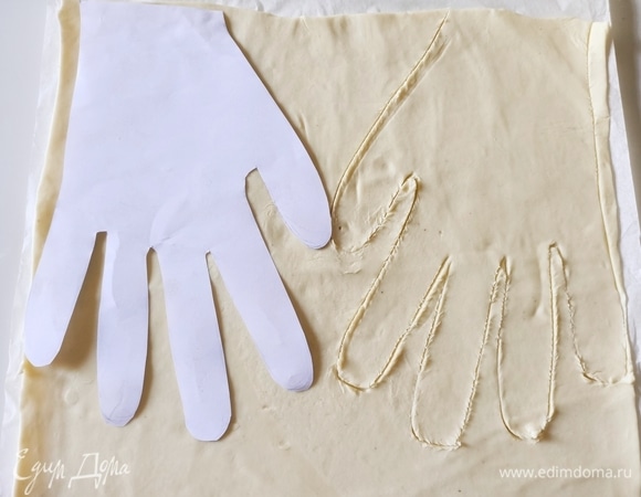На чистом листе бумаги нарисовать и вырезать руку. Раскатать слоеное тесто, приложить лекало и обвести ножом.