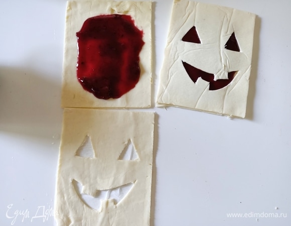 В центр прямоугольника положить варенье, смазать края молоком или водой, накрыть прямоугольником с вырезами для «рта» и «глаз». Закрепить края.