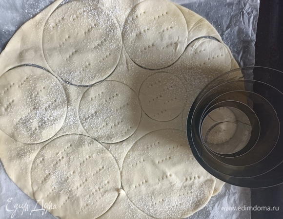 Я делаю круглые пирожные, но если вам нравится, то можно сделать квадратные или прямоугольные, все зависит от фантазии и купленного вами теста. Разогреваем духовку до 180°C. Разворачиваем готовое слоеное тесто, немного раскатываем и вырезаем круглые заготовки с помощью формочек или же стакана. Тесто прокалываем вилкой в нескольких местах, посыпаем сахарной пудрой и выпекаем в уже разогретой духовке в течение 10 минут до золотистого цвета. Готовые слоеные диски достаем из духовки и полностью остужаем.