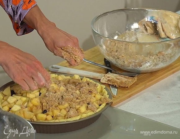 Вынуть форму из духовки, убрать с коржа бумагу с бобовыми, выложить на него яблочную начинку, сверху равномерно посыпать сливочно-ореховой крошкой и выпекать пирог еще около часа.    