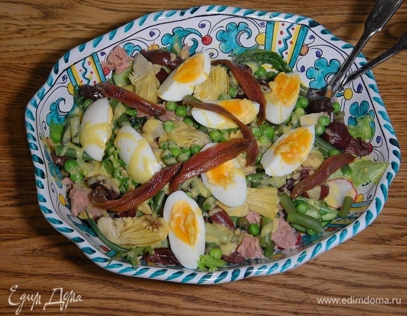 На овощи выложить кусочки тунца, артишоки, оливки, каперсы, стручковую фасоль, горошек и яйца, полить все оставшейся заправкой, сверху разложить анчоусы.