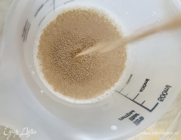 Молоко подогреваем до температуры 35–40°C. Заливаем дрожжи. В молоко добавляем пару ложек сахара. Перемешиваем. Накрываем полотенцем и убираем в сторону минут на 10.