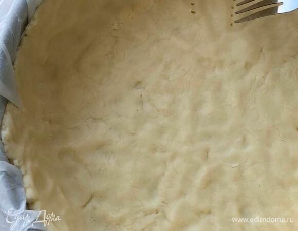 Форму застелите пергаментом, выложите тесто и сформируйте бортики до верха. Наколите тесто вилкой по всей площади и поставьте в разогретую духовку при 190°C на 15 минут.