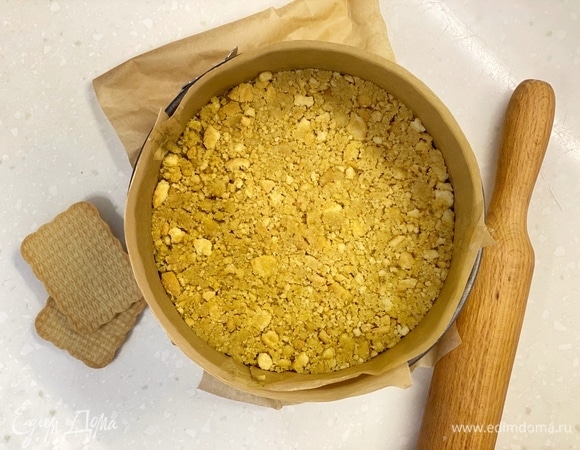 Печенье измельчить и смешать с растопленным маслом. Выложить смесь на дно формы, застеленной пергаментом. Убрать в холодильник.