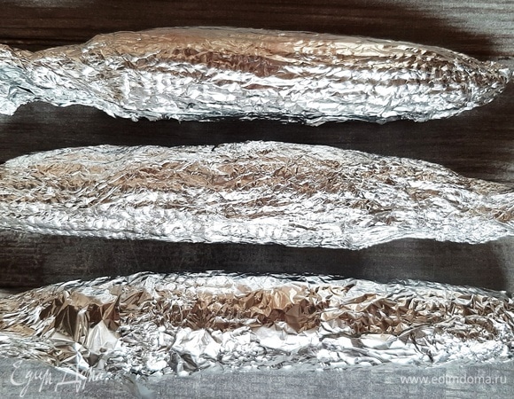 Каждый початок завернуть в фольгу. Сложить в форму для выпечки. Духовку разогреть до максимума. Ставим кукурузу в духовку и убавляем жар до 200°C. Запекаем 30 минут.