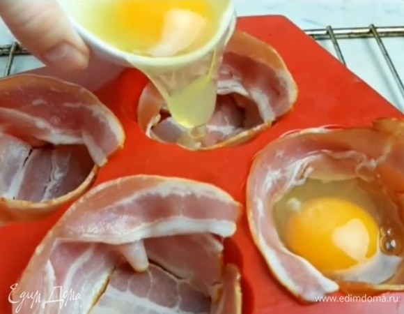 Выкладываем бекон по кругу формочки для кексов и кладем кусочек на дно. Разбиваем по одному яйцу в каждую формочку с беконом. 