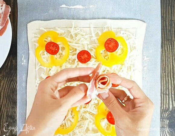 Равномерно распределяем сыр, далее кладем кольца перца и томаты. Ленты бекона скручиваем, формируя розочку, и выкладываем на пирог. Выпекаем в хорошо прогретой духовке при температуре 200°С около 20 минут. Ориентируйтесь по румяности.